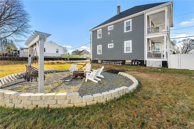 rear view of house featuring a fire pit, a balcony, and a yard