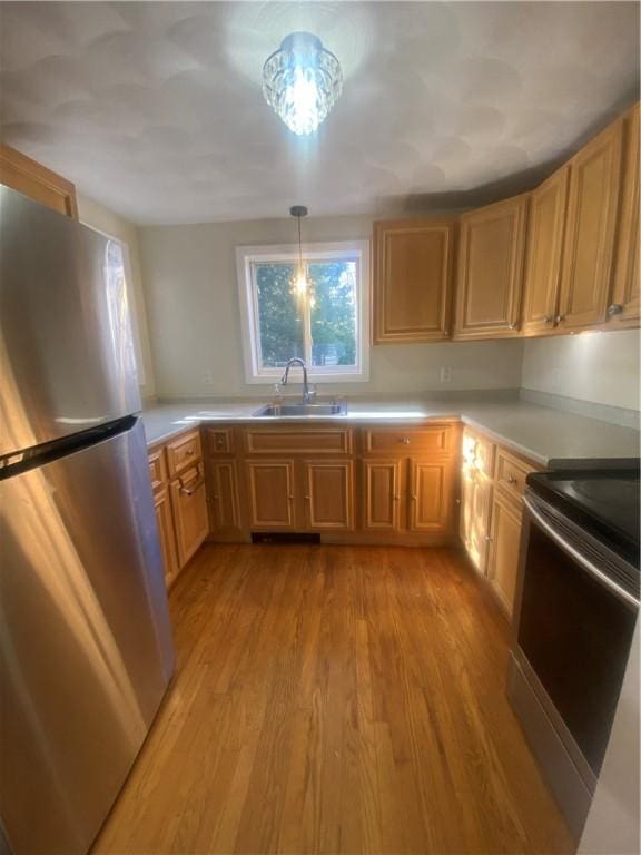 kitchen with appliances with stainless steel finishes, light countertops, a sink, and light wood finished floors