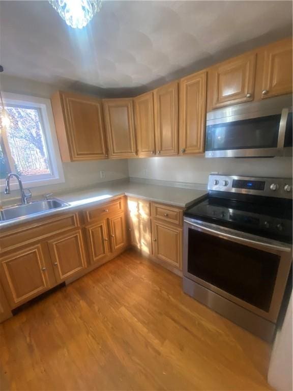 kitchen featuring light wood-style floors, appliances with stainless steel finishes, light countertops, and a sink