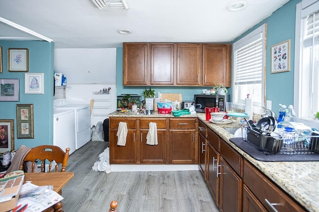 kitchen featuring independent washer and dryer, light hardwood / wood-style floors, and light stone counters