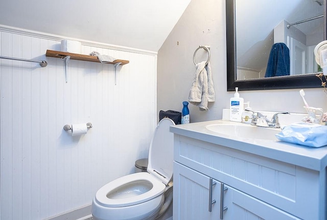 bathroom featuring wood walls, vanity, lofted ceiling, and toilet