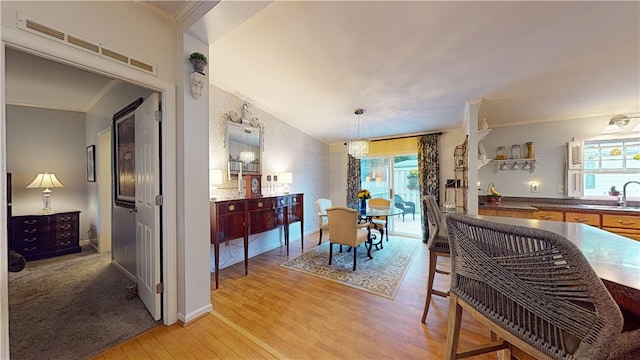 dining room featuring a chandelier, ornamental molding, sink, and light hardwood / wood-style flooring