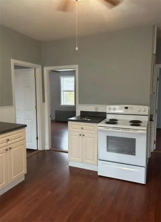 kitchen featuring white range with electric stovetop, a ceiling fan, radiator, dark wood-style floors, and dark countertops