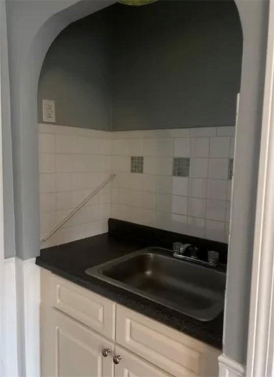 kitchen featuring arched walkways, dark countertops, a sink, and white cabinets