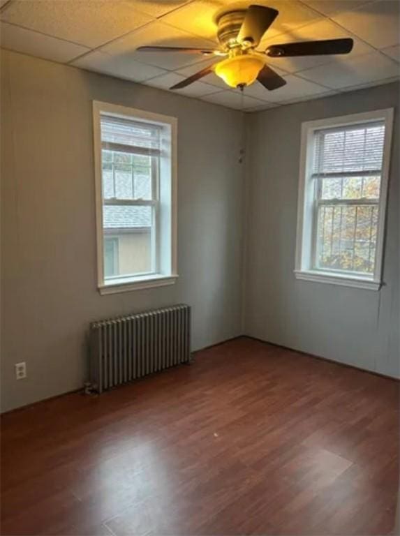 unfurnished room featuring hardwood / wood-style floors, a drop ceiling, ceiling fan, and radiator heating unit