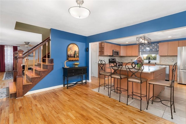 kitchen featuring sink, tasteful backsplash, light hardwood / wood-style flooring, decorative light fixtures, and appliances with stainless steel finishes