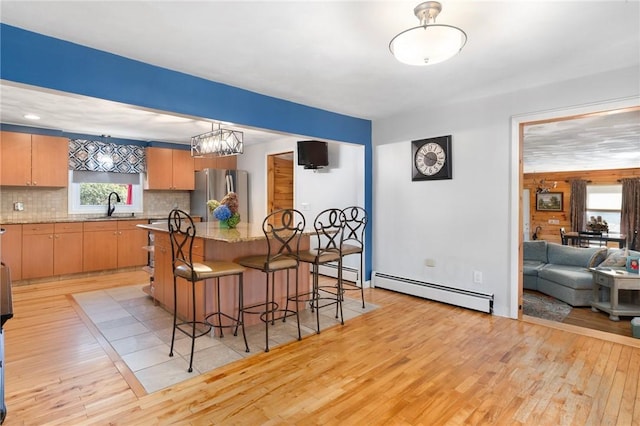 kitchen featuring tasteful backsplash, a breakfast bar, sink, a baseboard radiator, and stainless steel refrigerator