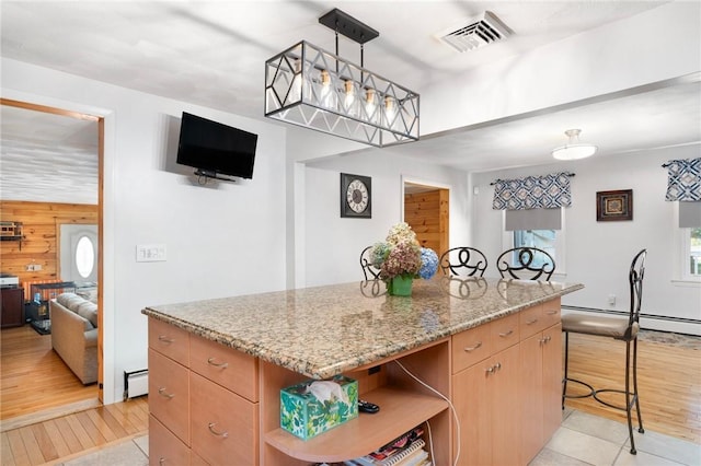 kitchen with wood walls, a center island, light stone counters, and a baseboard heating unit