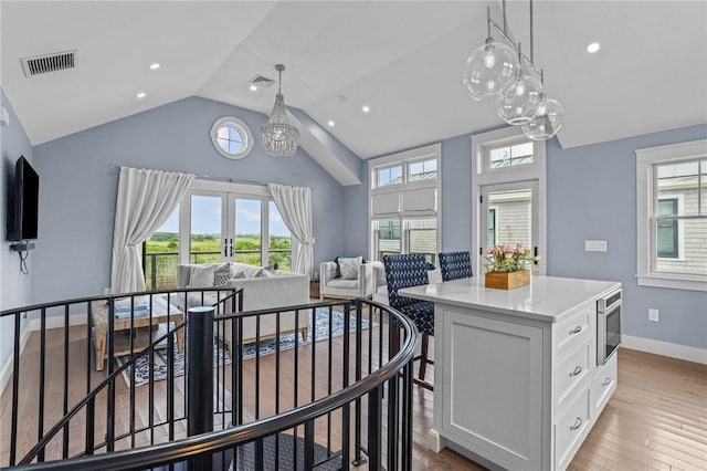 kitchen featuring a center island, lofted ceiling, white cabinets, hanging light fixtures, and light wood-type flooring