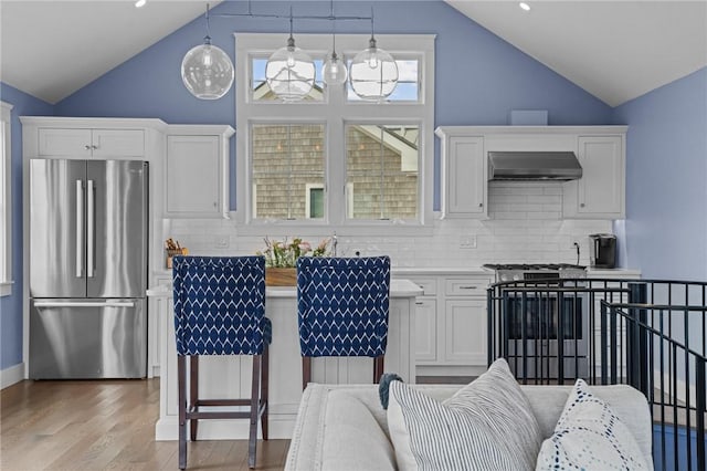 kitchen featuring pendant lighting, decorative backsplash, range hood, white cabinetry, and stainless steel refrigerator