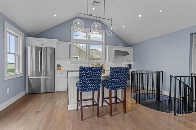 kitchen featuring pendant lighting, wall chimney range hood, decorative backsplash, stainless steel fridge, and white cabinetry