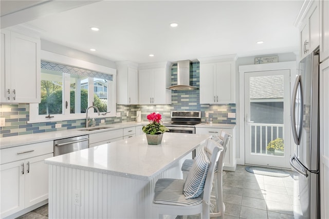 kitchen with wall chimney exhaust hood, stainless steel appliances, sink, white cabinets, and a center island