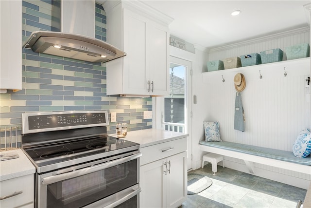 kitchen with wall chimney range hood, backsplash, white cabinetry, and stainless steel range oven