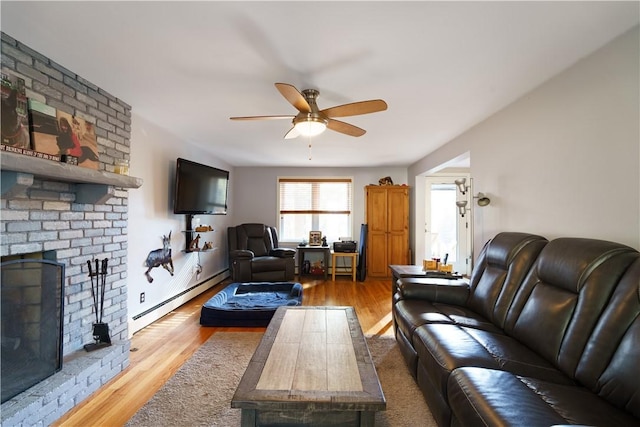 living room with a brick fireplace, a baseboard radiator, light hardwood / wood-style flooring, and ceiling fan