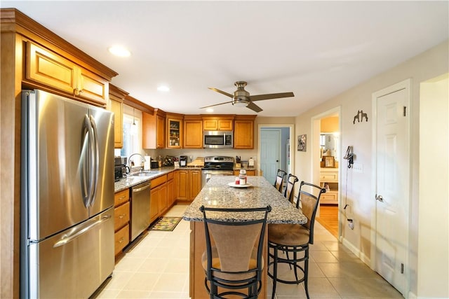 kitchen with ceiling fan, light stone countertops, stainless steel appliances, a breakfast bar area, and a kitchen island