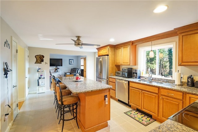 kitchen featuring ceiling fan, sink, stainless steel appliances, a breakfast bar, and a kitchen island