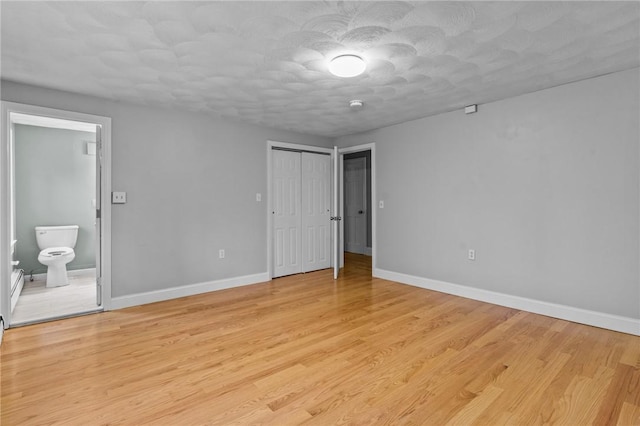 unfurnished bedroom with connected bathroom, a textured ceiling, light hardwood / wood-style floors, and a closet