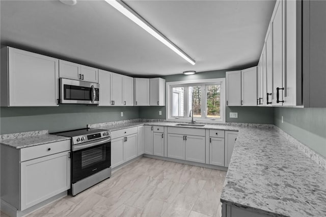 kitchen with appliances with stainless steel finishes, sink, white cabinets, and light stone counters