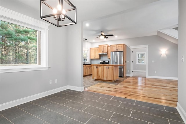 kitchen with stainless steel fridge, light brown cabinetry, hanging light fixtures, and ceiling fan with notable chandelier