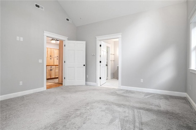 unfurnished bedroom with connected bathroom, light carpet, and high vaulted ceiling