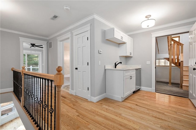 kitchen featuring stainless steel dishwasher, ceiling fan, light wood-type flooring, ornamental molding, and white cabinetry