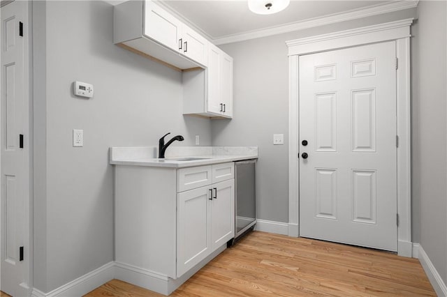 laundry area with sink, light hardwood / wood-style flooring, and ornamental molding