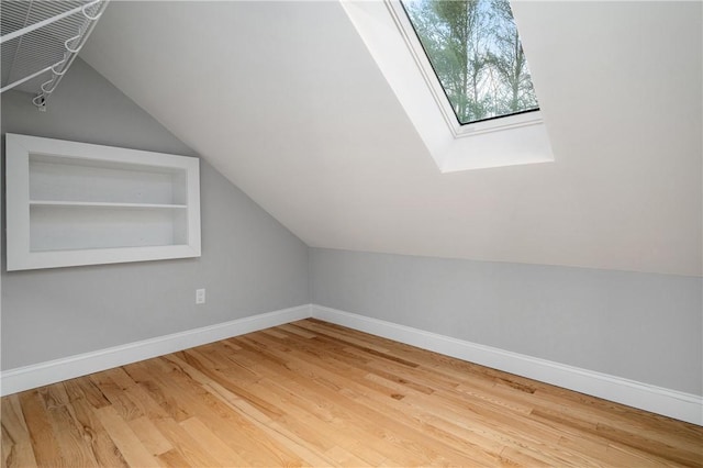 bonus room with built in shelves, wood-type flooring, and lofted ceiling with skylight