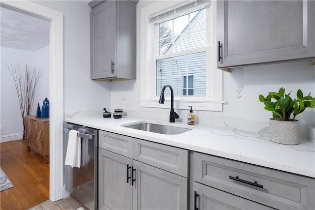 kitchen featuring light stone counters, sink, light hardwood / wood-style flooring, dishwasher, and gray cabinets