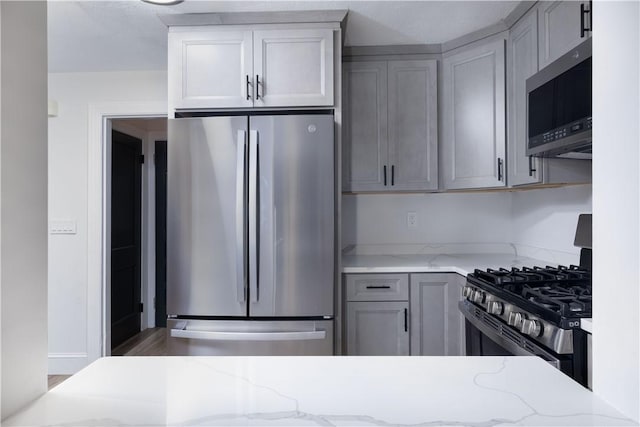 kitchen featuring gray cabinets, light stone countertops, stainless steel appliances, and hardwood / wood-style flooring