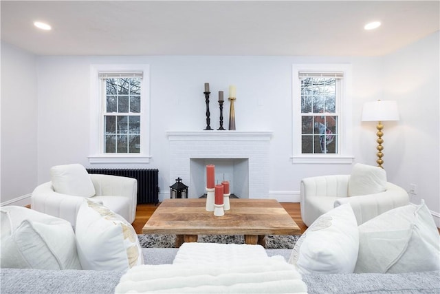 living room featuring radiator, hardwood / wood-style floors, and a brick fireplace