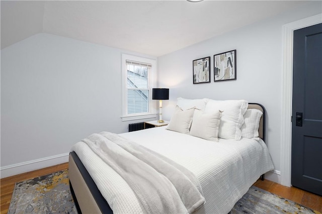 bedroom featuring wood-type flooring, vaulted ceiling, and radiator