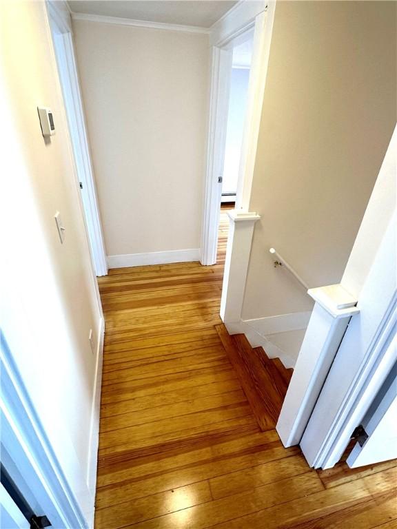 hallway with baseboard heating, ornamental molding, and light wood-type flooring