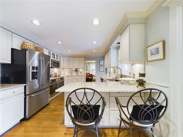 kitchen with kitchen peninsula, light stone counters, stainless steel appliances, sink, and white cabinets