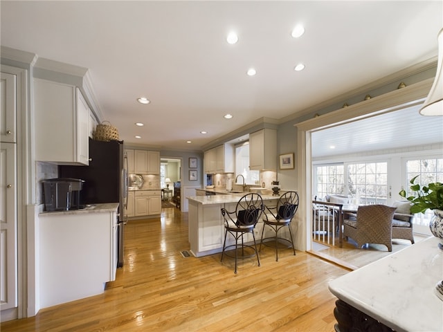 kitchen with light wood-type flooring, backsplash, a breakfast bar area, and ornamental molding