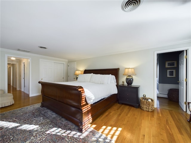 bedroom featuring a closet, light hardwood / wood-style floors, baseboard heating, and ornamental molding