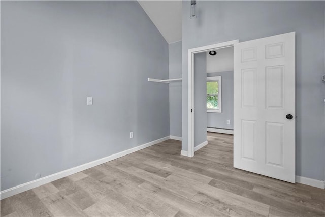 empty room featuring a baseboard radiator, vaulted ceiling, and light hardwood / wood-style floors