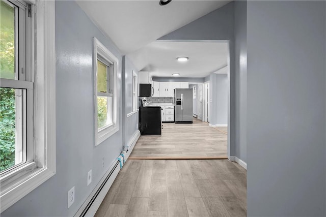 hallway with a wealth of natural light, vaulted ceiling, and light wood-type flooring