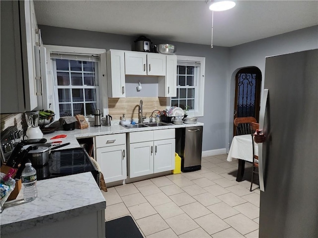 kitchen featuring decorative backsplash, appliances with stainless steel finishes, sink, light tile patterned floors, and white cabinets