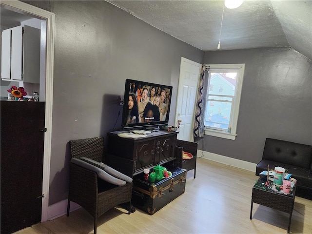 sitting room with lofted ceiling, light wood-type flooring, and a textured ceiling