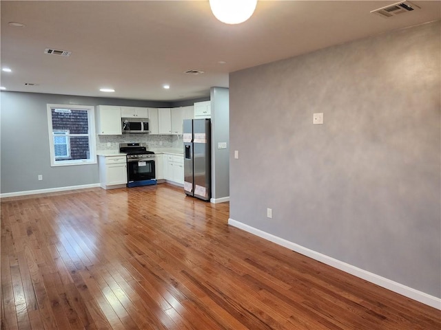 kitchen with white cabinets, tasteful backsplash, stainless steel appliances, and hardwood / wood-style floors