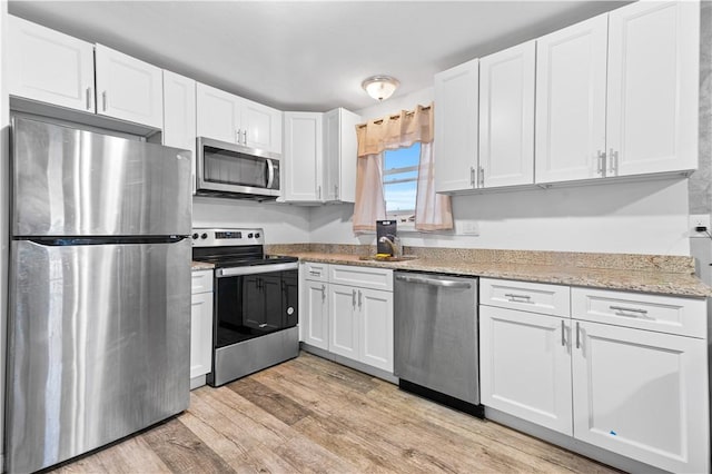 kitchen featuring white cabinets, appliances with stainless steel finishes, light hardwood / wood-style floors, and light stone counters