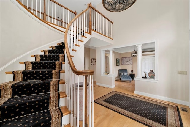 stairway with a towering ceiling, hardwood / wood-style flooring, and ornate columns