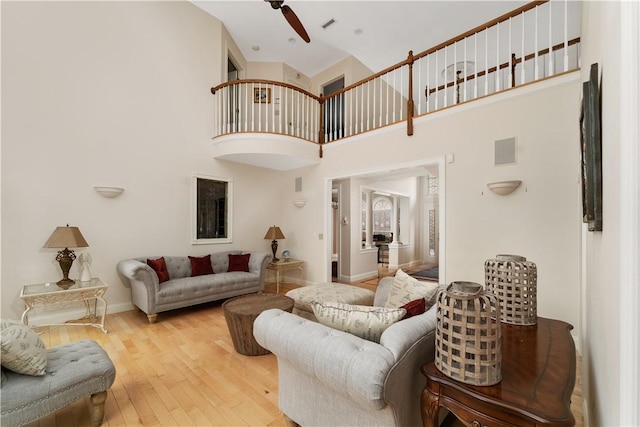 living room with a high ceiling, ceiling fan, and wood-type flooring