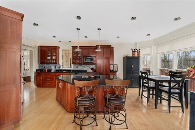 kitchen featuring stainless steel microwave, a center island, hanging light fixtures, tasteful backsplash, and light hardwood / wood-style flooring