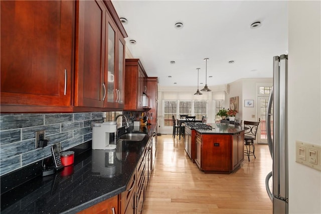 kitchen with dark stone counters, ornamental molding, sink, a kitchen island, and hanging light fixtures