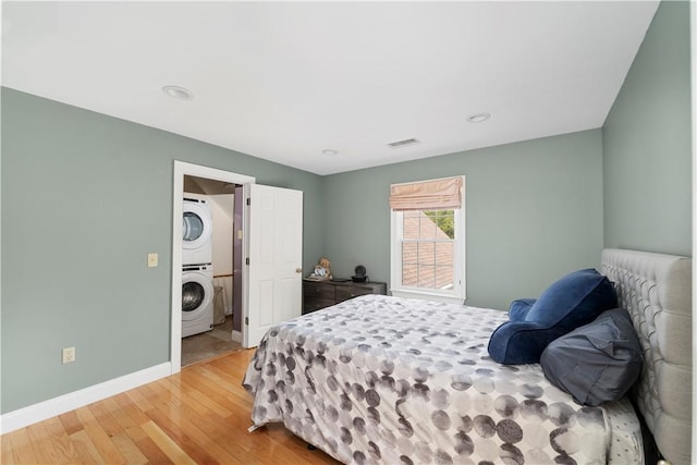 bedroom featuring hardwood / wood-style flooring and stacked washer / dryer