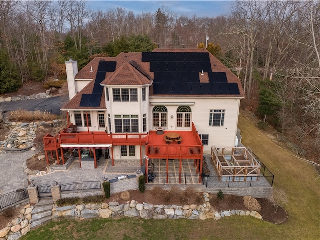 rear view of house with a wooden deck, a patio, and solar panels