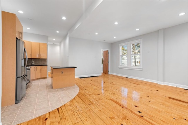 kitchen with light brown cabinets, backsplash, stainless steel refrigerator with ice dispenser, light wood-type flooring, and a kitchen island