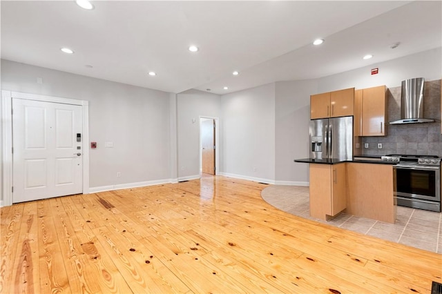 kitchen featuring a center island, wall chimney exhaust hood, light wood-type flooring, appliances with stainless steel finishes, and tasteful backsplash