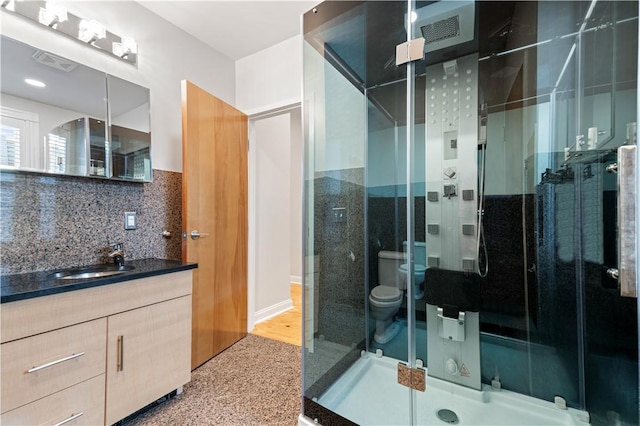 bathroom featuring vanity, toilet, decorative backsplash, and walk in shower